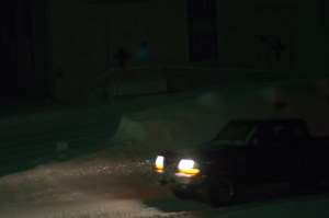 Photo of a truck driving in the snow at night.