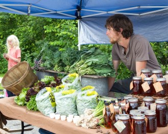 Andy Paonessa of Heartwood Farm in South Albany works his stand at the Montpelier Farmers Market in June. Looking on is Samual Robb of Tangletown Farm. Photo by Roger Crowley for VTDigger