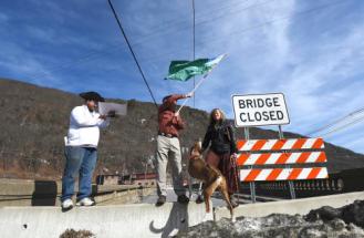 Emily Peyton (right), Mike Smith and Torin Brooks (left) stand on a barricade before reciting a declaration claiming the Vilas Bridge for the state of Vermont on Tuesday afternoon. Photo by Kayla Rice/BrattleboroReformer 