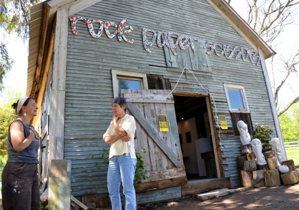Thea Alvin (left) chats with a visitor to her studio in an old 1810 barn on her homestead. The sign is made of carved wood and decorated with bottle caps. Photo by Andrew Nemethy