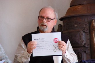 Elmore school board member Stuart Weppler holds up a sign to show the steps from a merger study to an eventual vote of the electorate, at the annual Elmore Town Meeting on Tuesday.