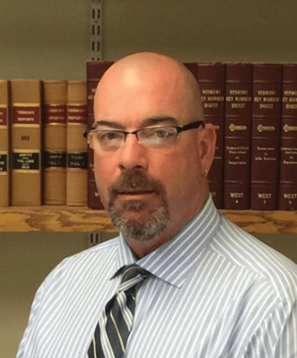 A bald man standing in front of a book shelf.
