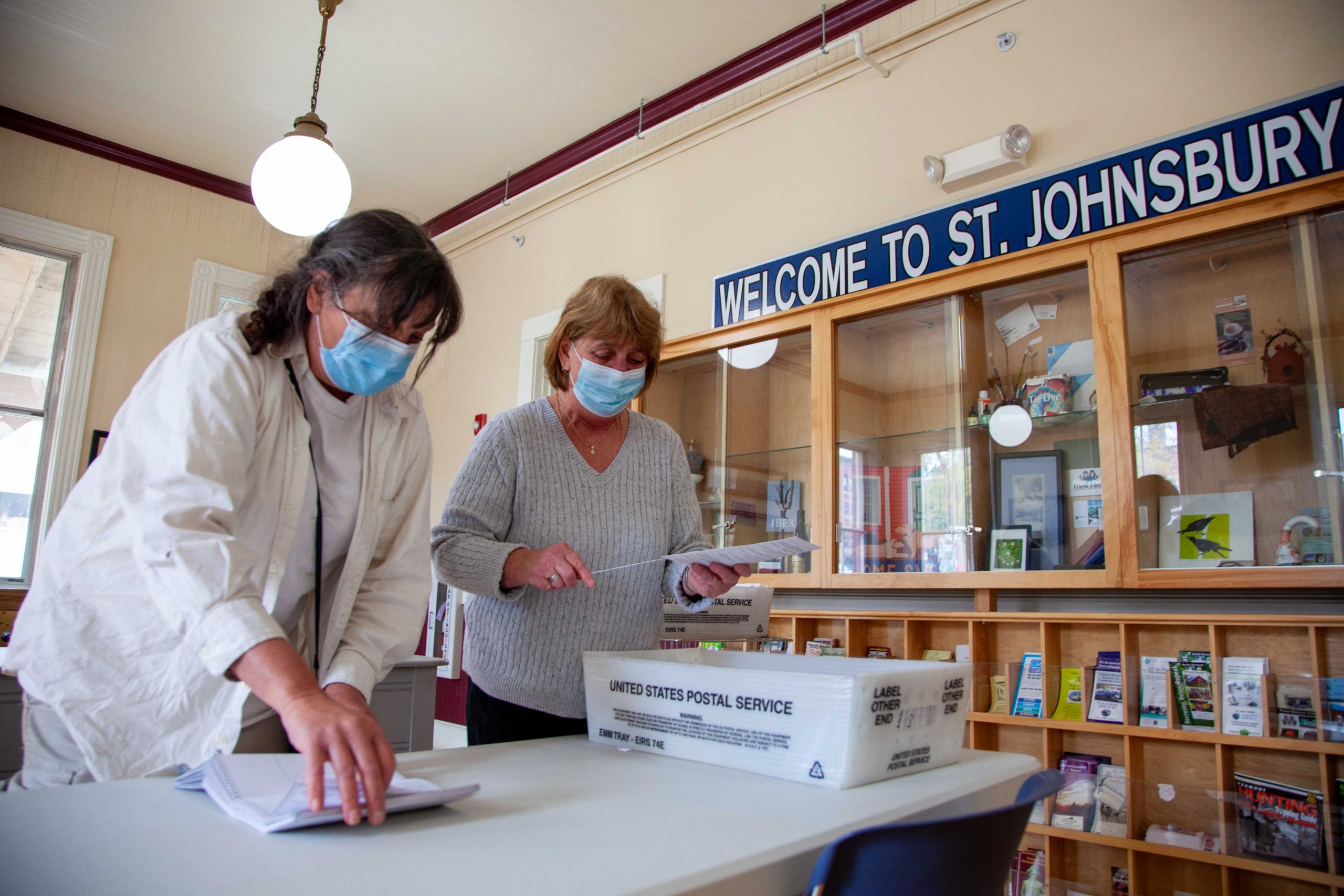Sue Haney and Diane Perkins open ballots in front of St. Johnsbury sign