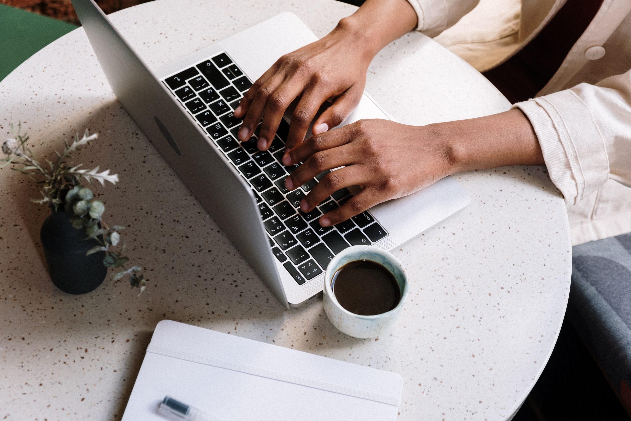 A person types on their laptop with a cup of black coffee nearby.