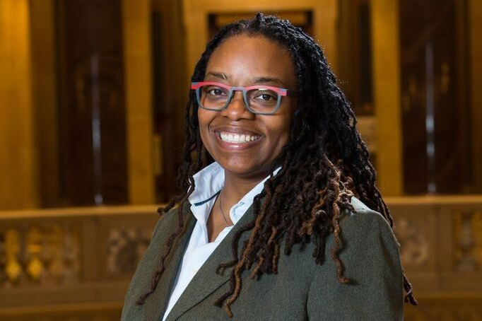 A woman with glasses smiling in front of a building.