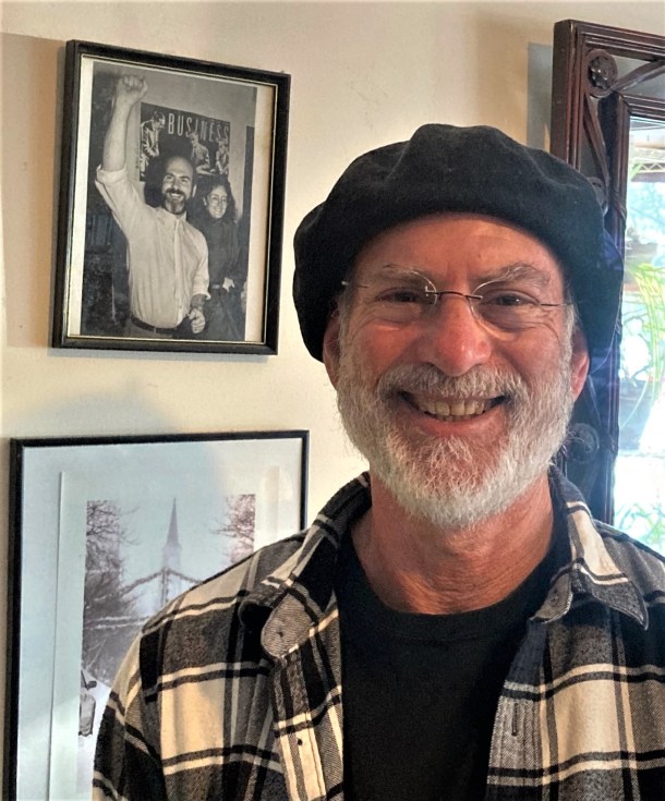 A man smiling in a room with framed pictures.