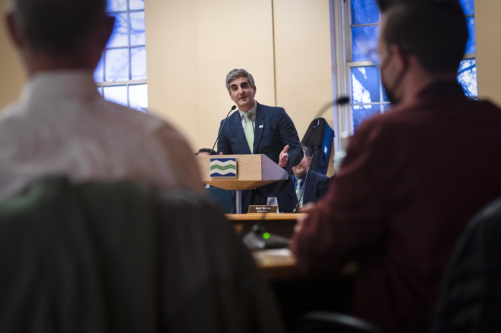 A man in a suit talks to silhouetted people across the room.