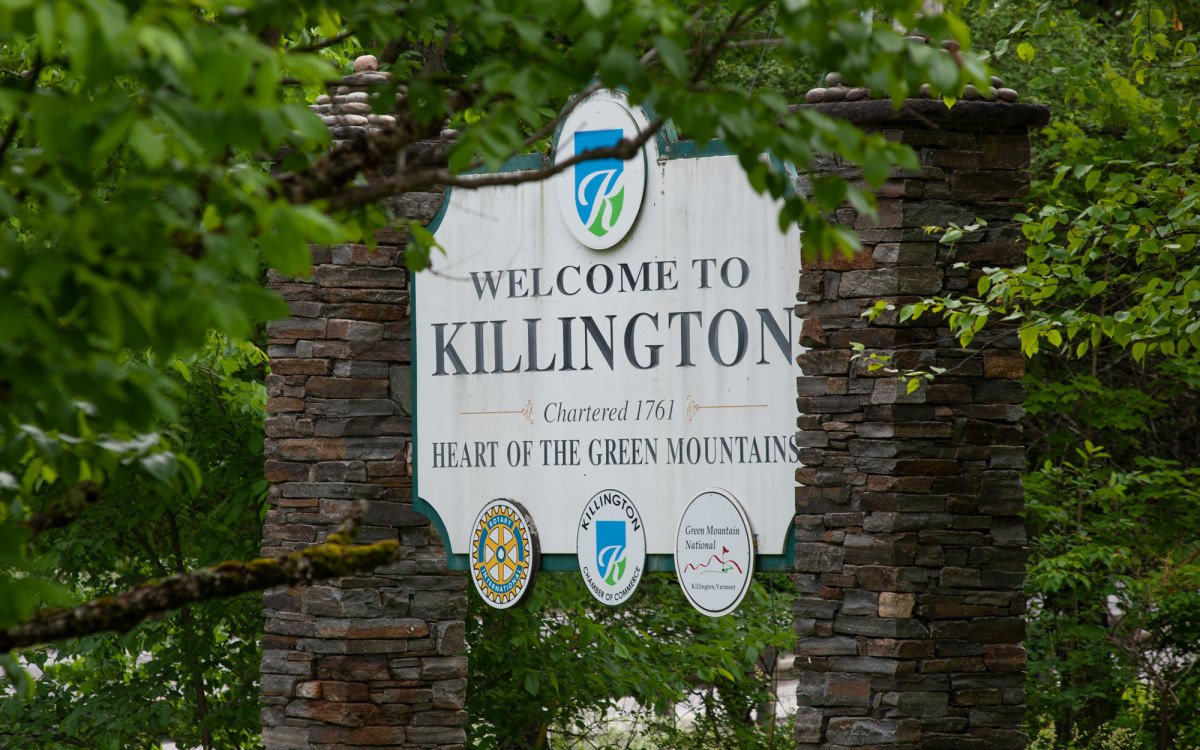 A stone sign reading "Welcome to Killington, Chartered 1761, Heart of the Green Mountains" is partially obscured by green foliage.