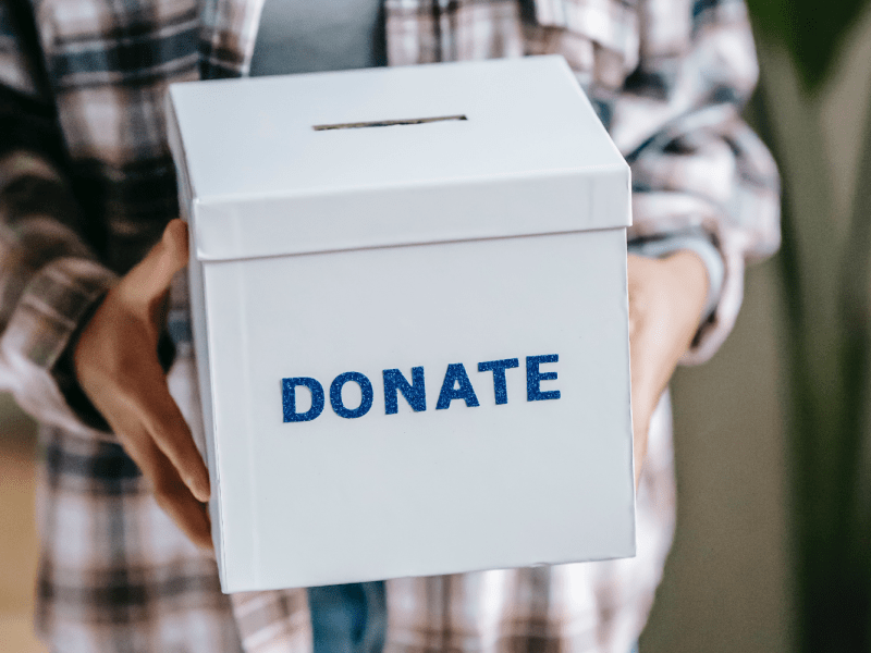 A person holds a box with blue letters that read "Donate."