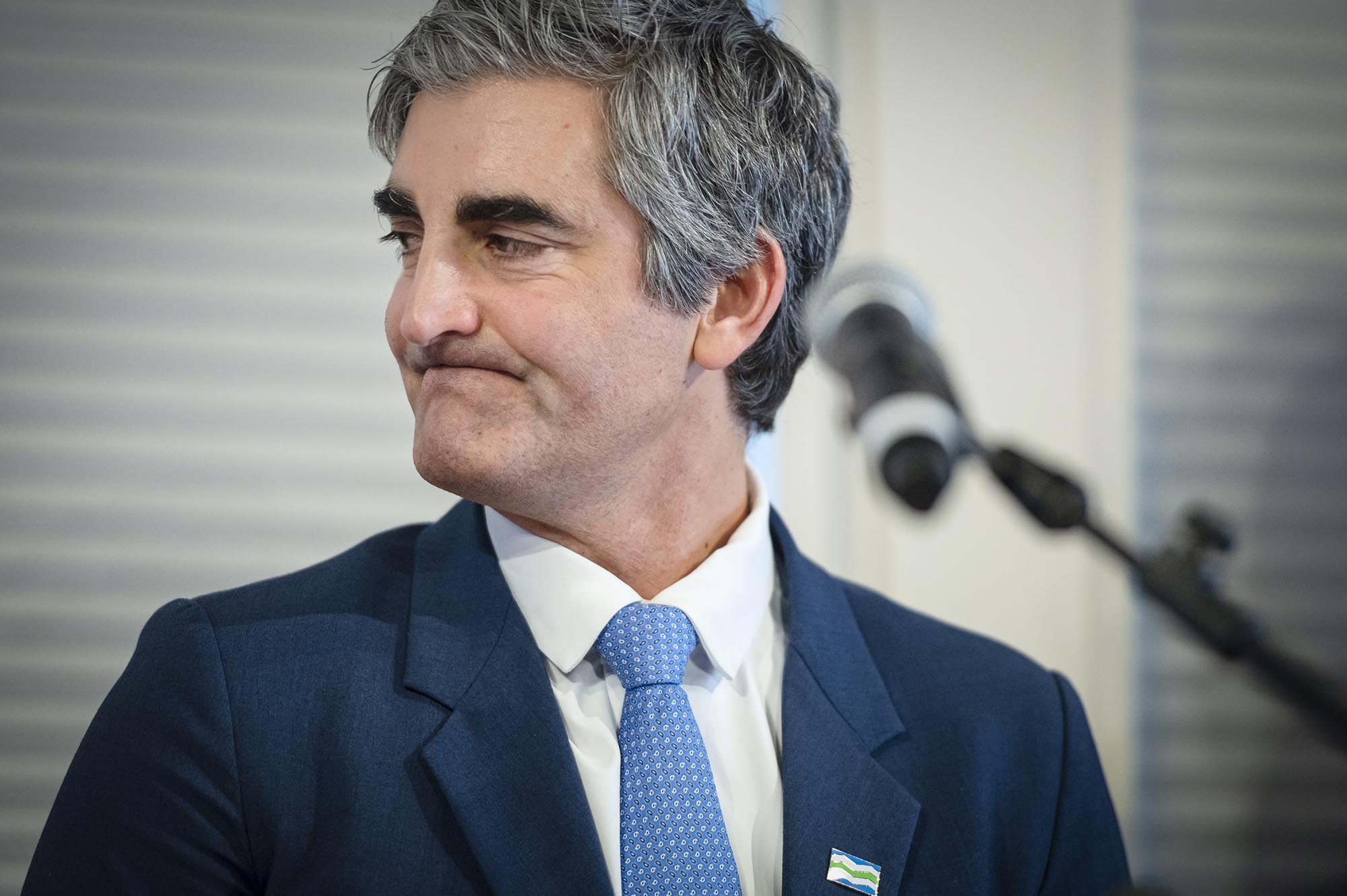A man in a suit and tie smiles into a microphone.