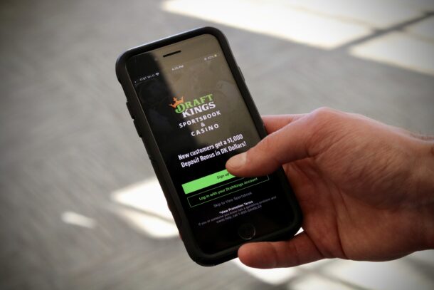 A hand holds a smartphone displaying the DraftKings Sportsbook & Casino app, showing a sign-up offer for new customers.