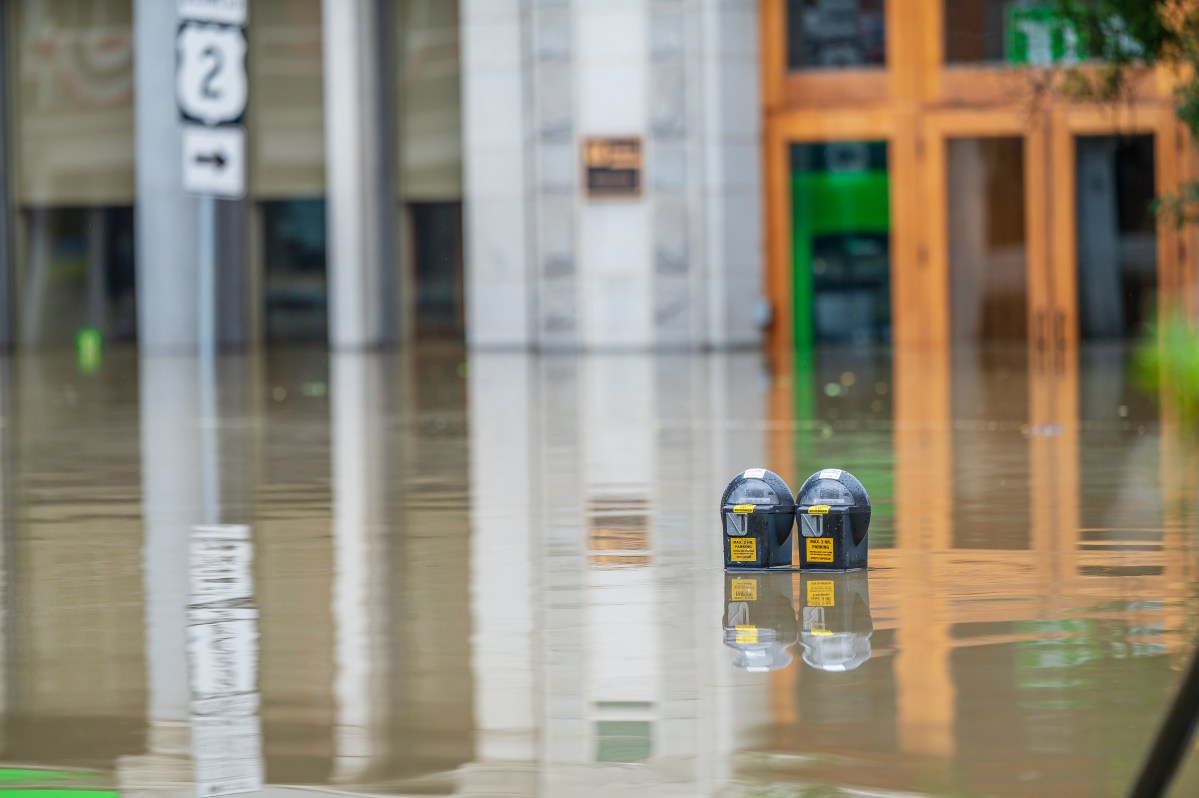 the top of a parking meter is visible in a flooded area in front of a building.