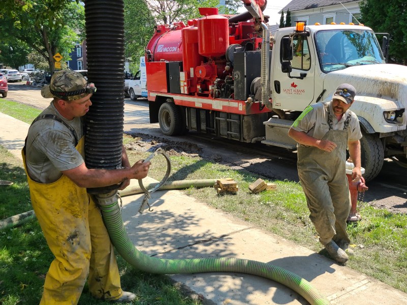 two men working on a hose on a street.