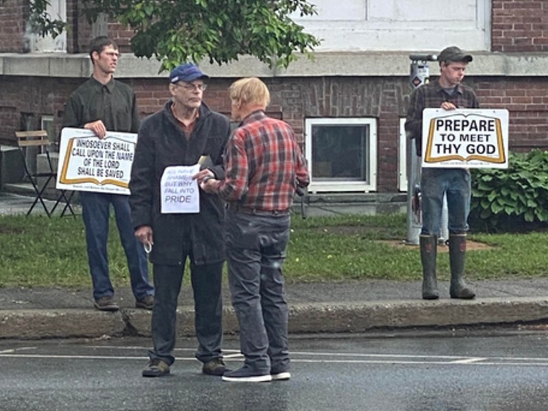 a group of people standing on a street holding signs. one reads "prepare to meet thy God."