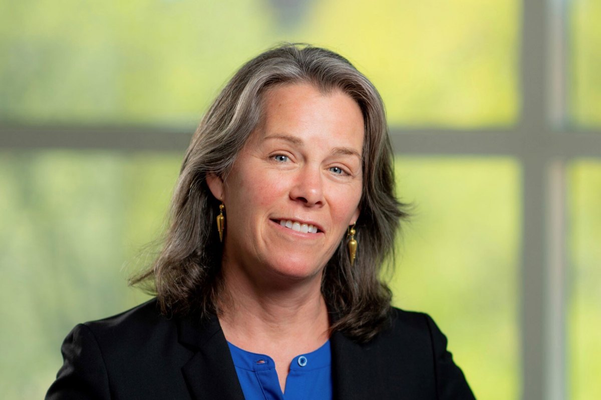 a woman in a blue shirt is smiling in front of a window.