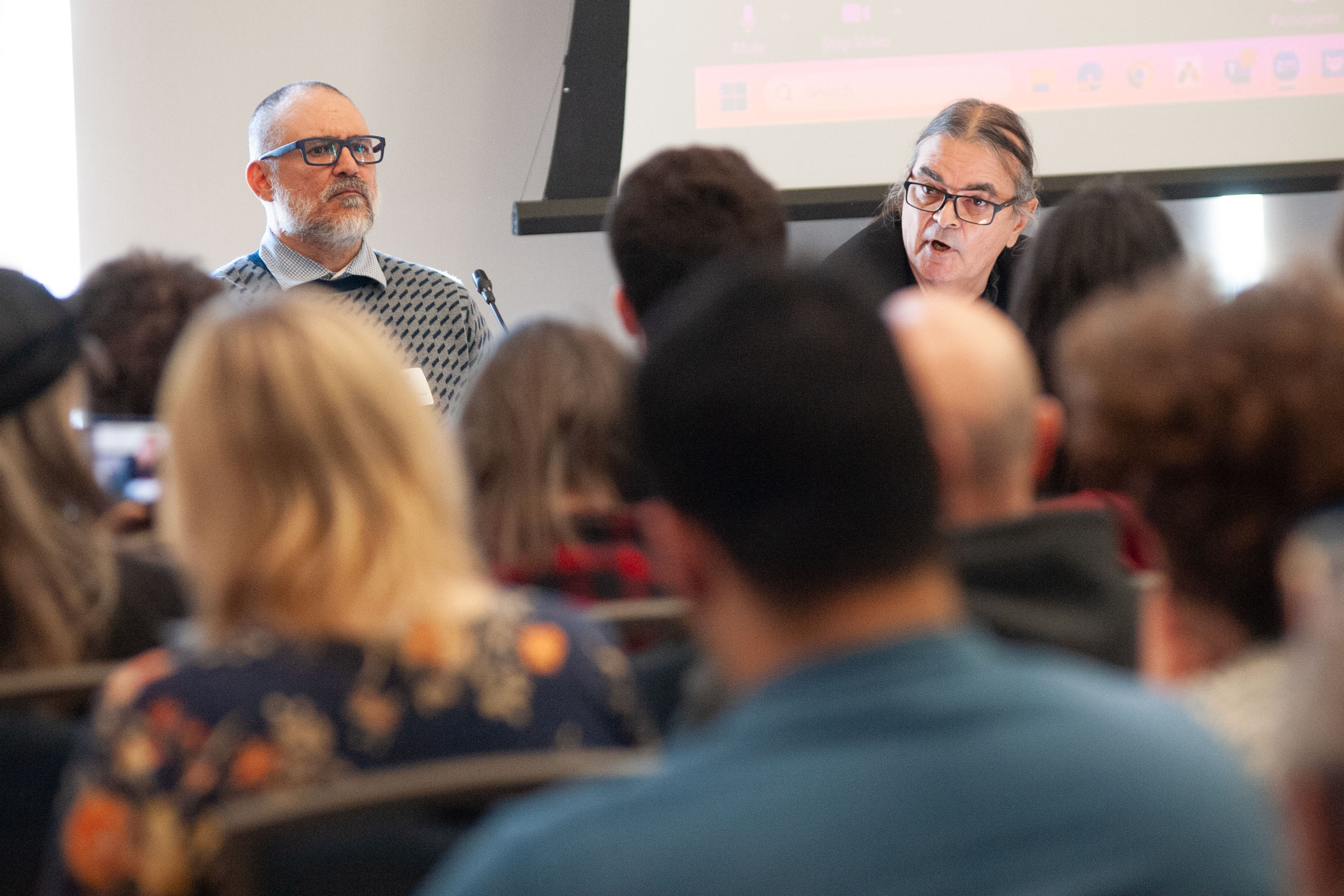 Two panelists speak in front of a crowd.