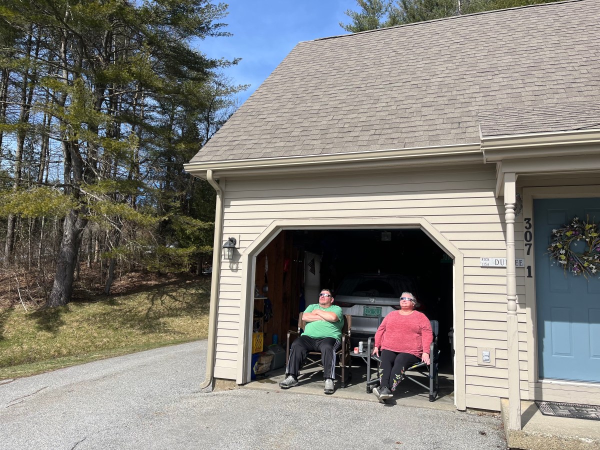 Two individuals sitting in a garage by an open door on a sunny day.