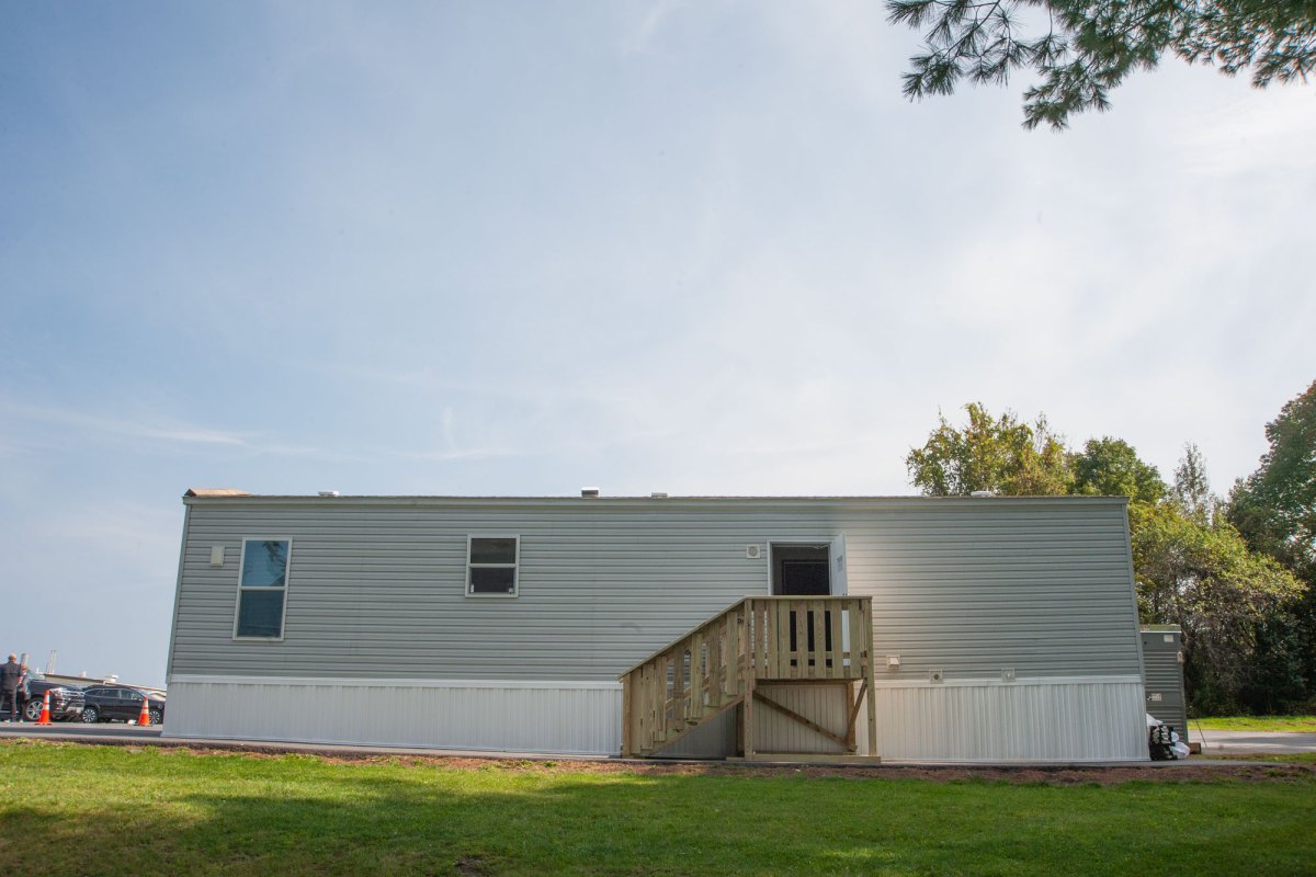 A manufactured home sits next to grass and trees.