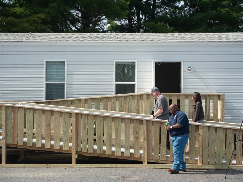 People walk up a ramp to a manufactured home.