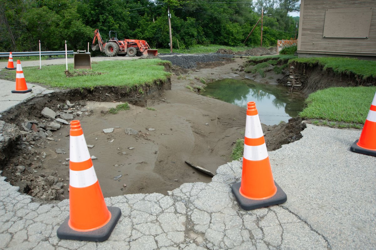 Orange traffic cones around a sink hole with an orange excavator in the background.
