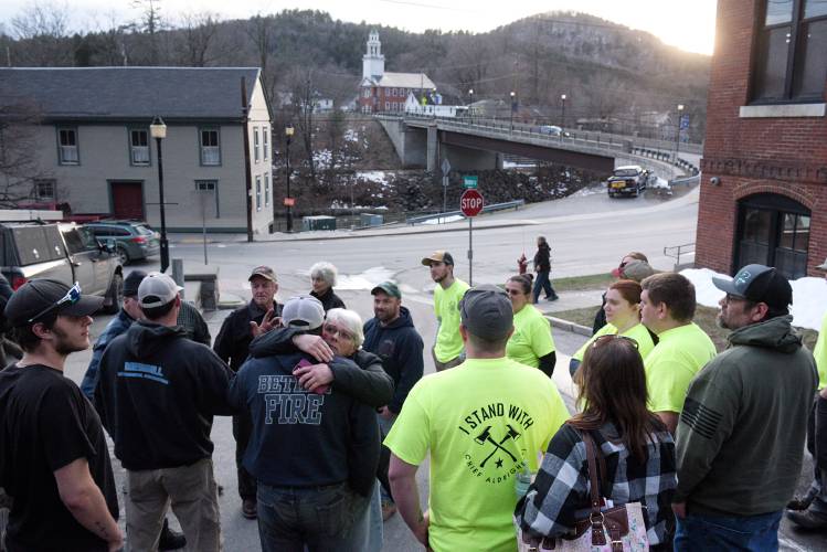 Woman hugs man as others gather around outside in a small town