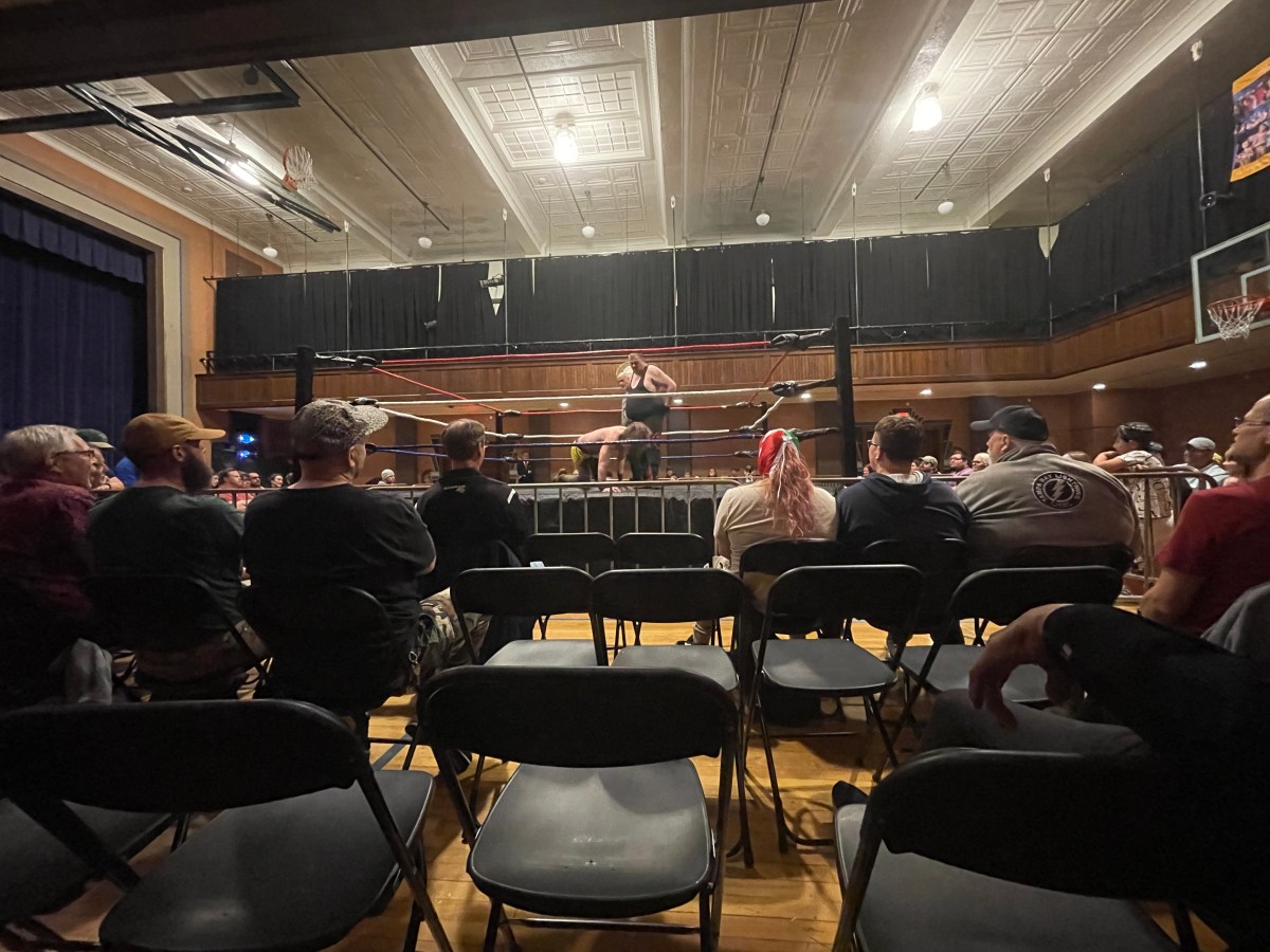 a group of people sitting in chairs in a room watching a wrestling ring in the middle