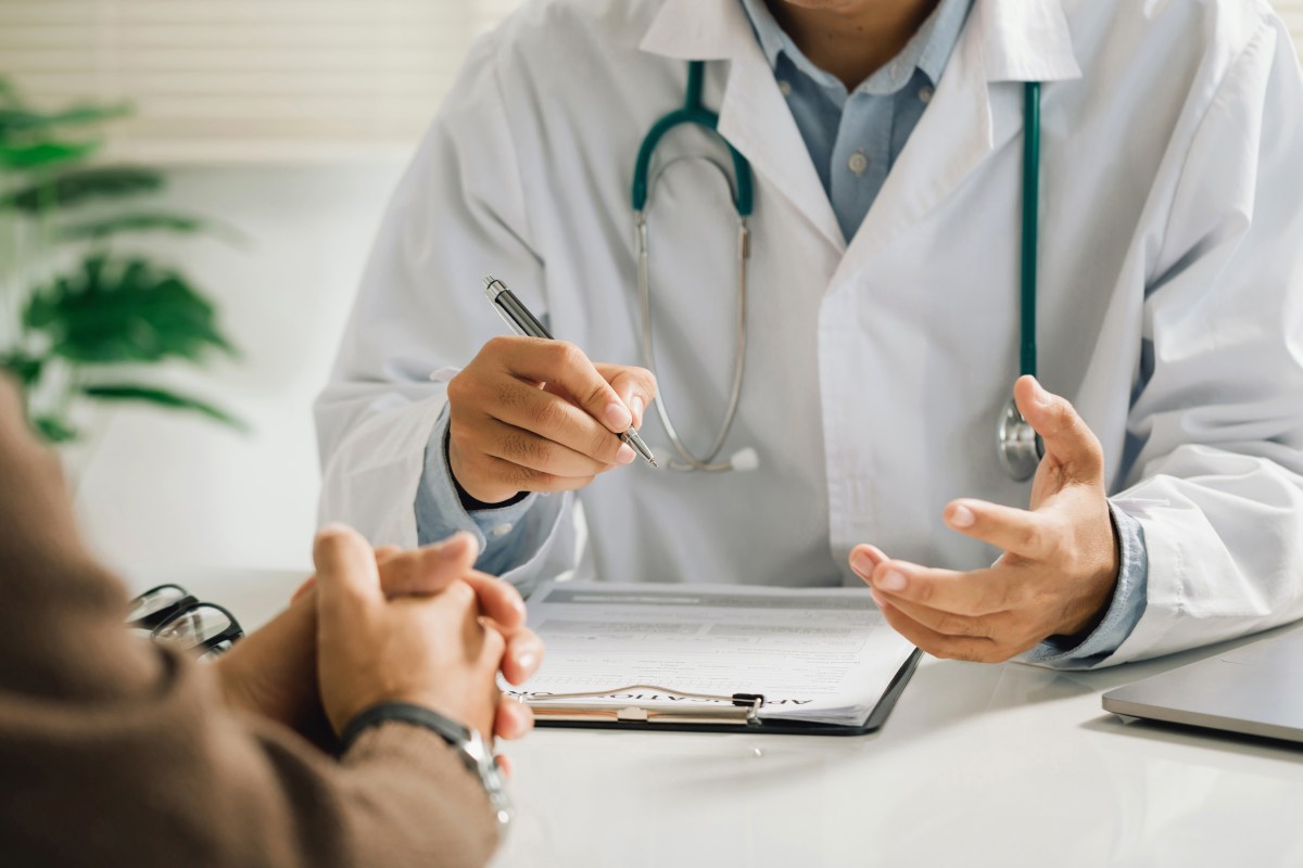 A doctor in a white coat and stethoscope talks to a patient.
