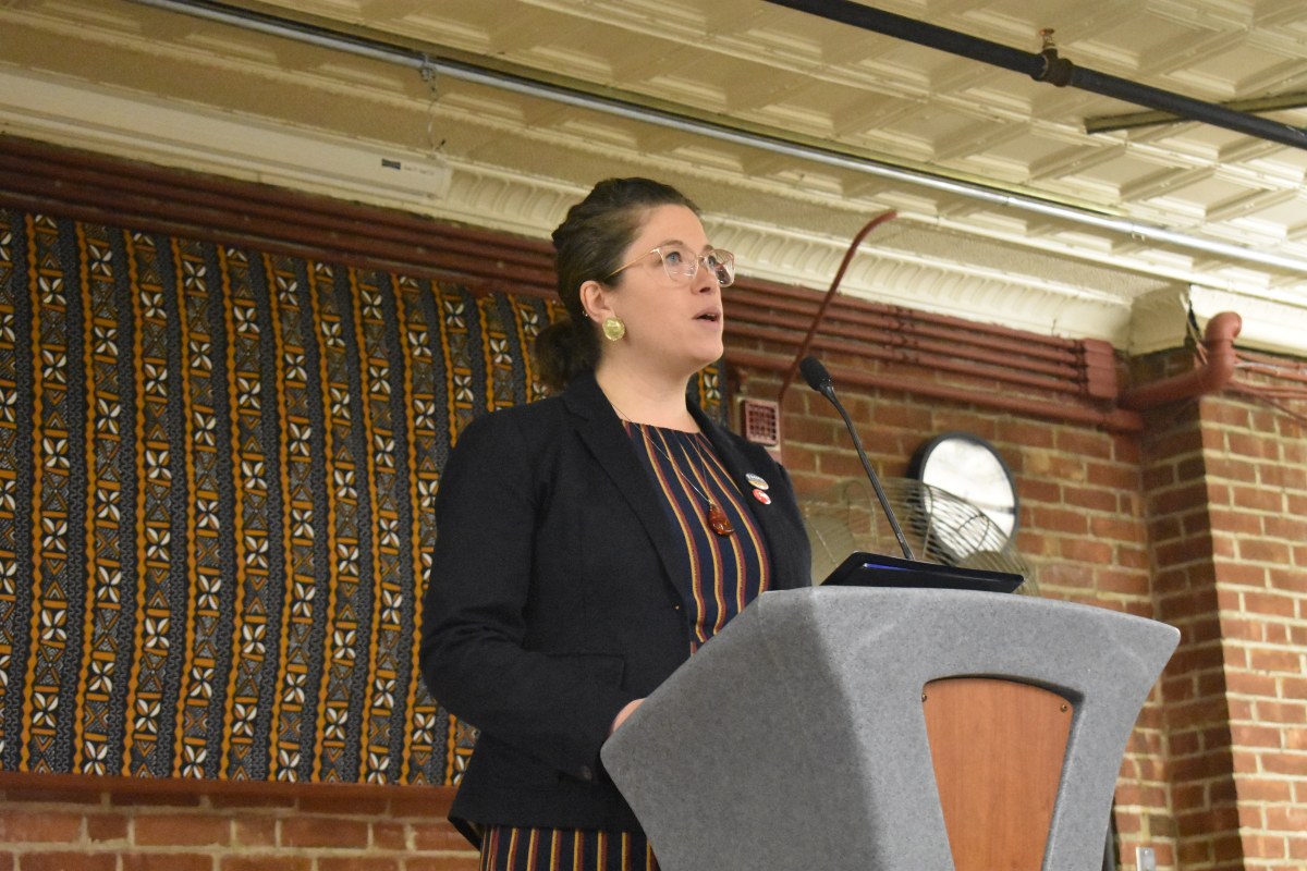 A woman standing at a podium in front of a brick wall.