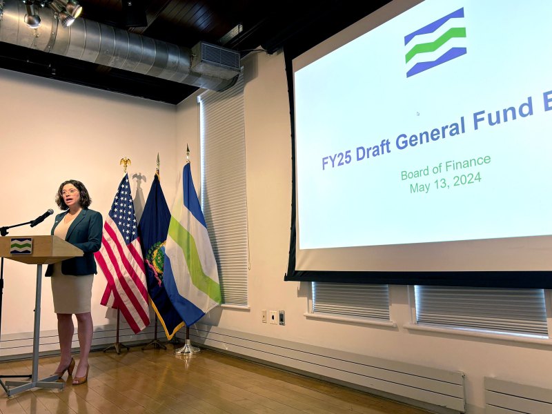A woman speaks at a podium in front of a projected screen.