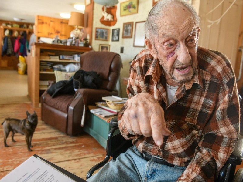 An elderly man in a wheelchair reading a book.