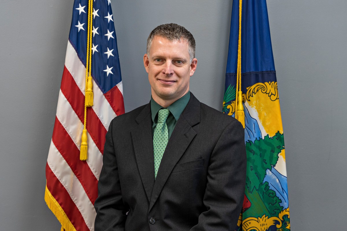 A man in a suit and tie standing in front of two flags.