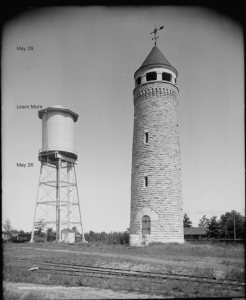 An old photo of a water tower next to a train track.