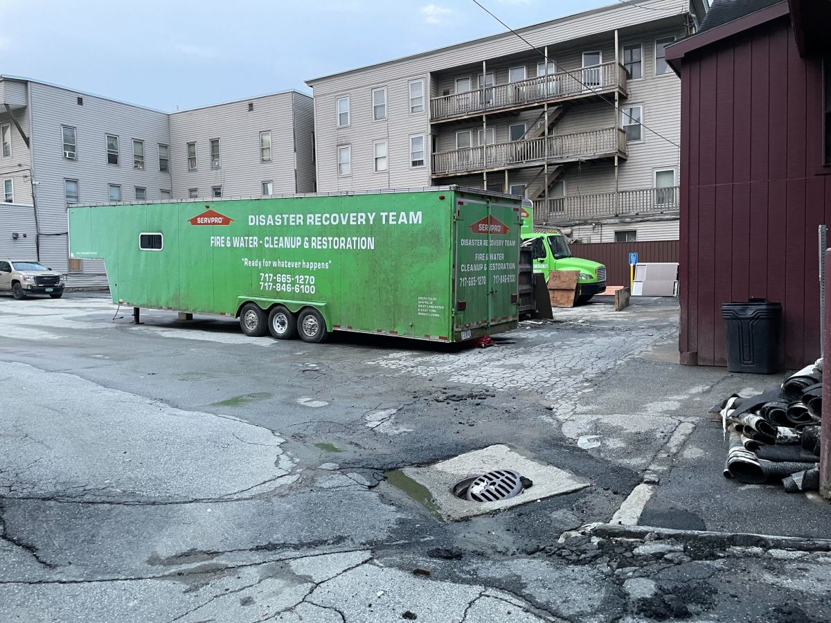 A green dumpster is parked in front of a building.