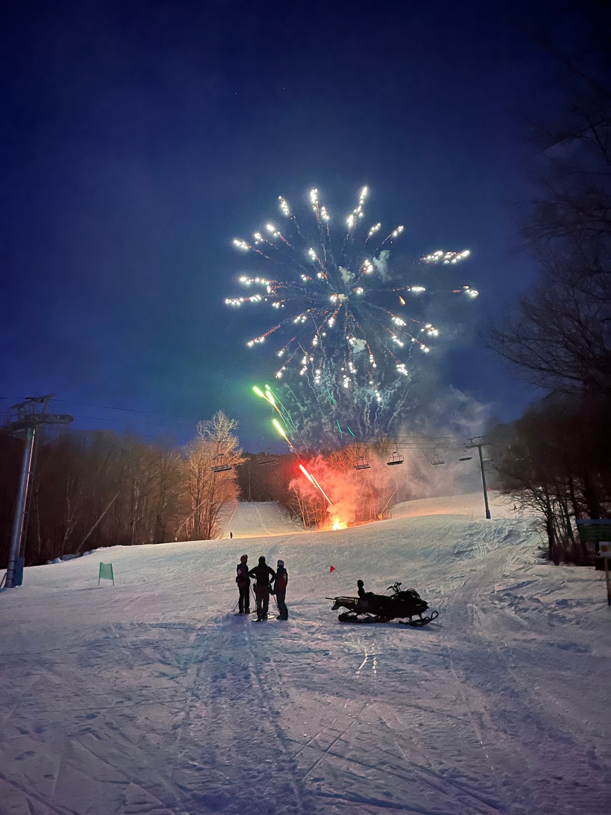 People standing on a snowy hill with fireworks in the sky.