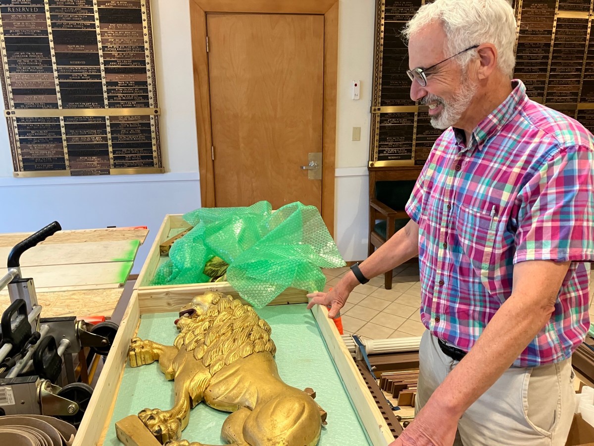 An older man looking at a gold lion in a box.