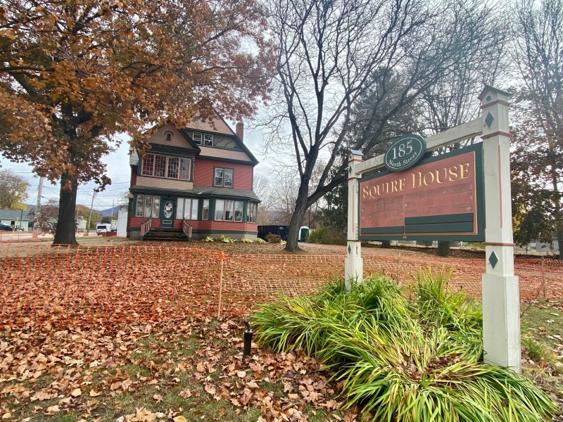 A sign in front of a house with leaves on it.