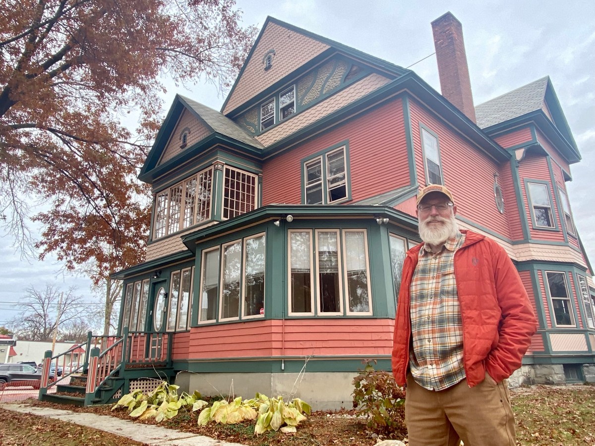 A man standing in front of a pink victorian house.