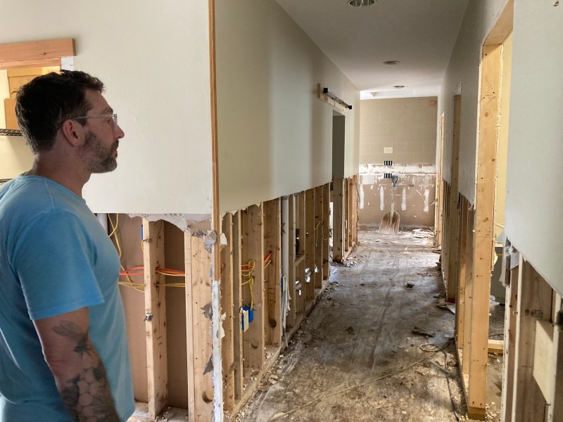 A man in a blue shirt looks down a hallway that's been partially demolished.
