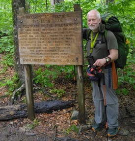 A man with a backpack standing next to a sign in the woods.