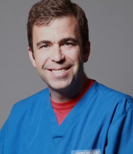 A man in blue scrubs smiling for the camera.