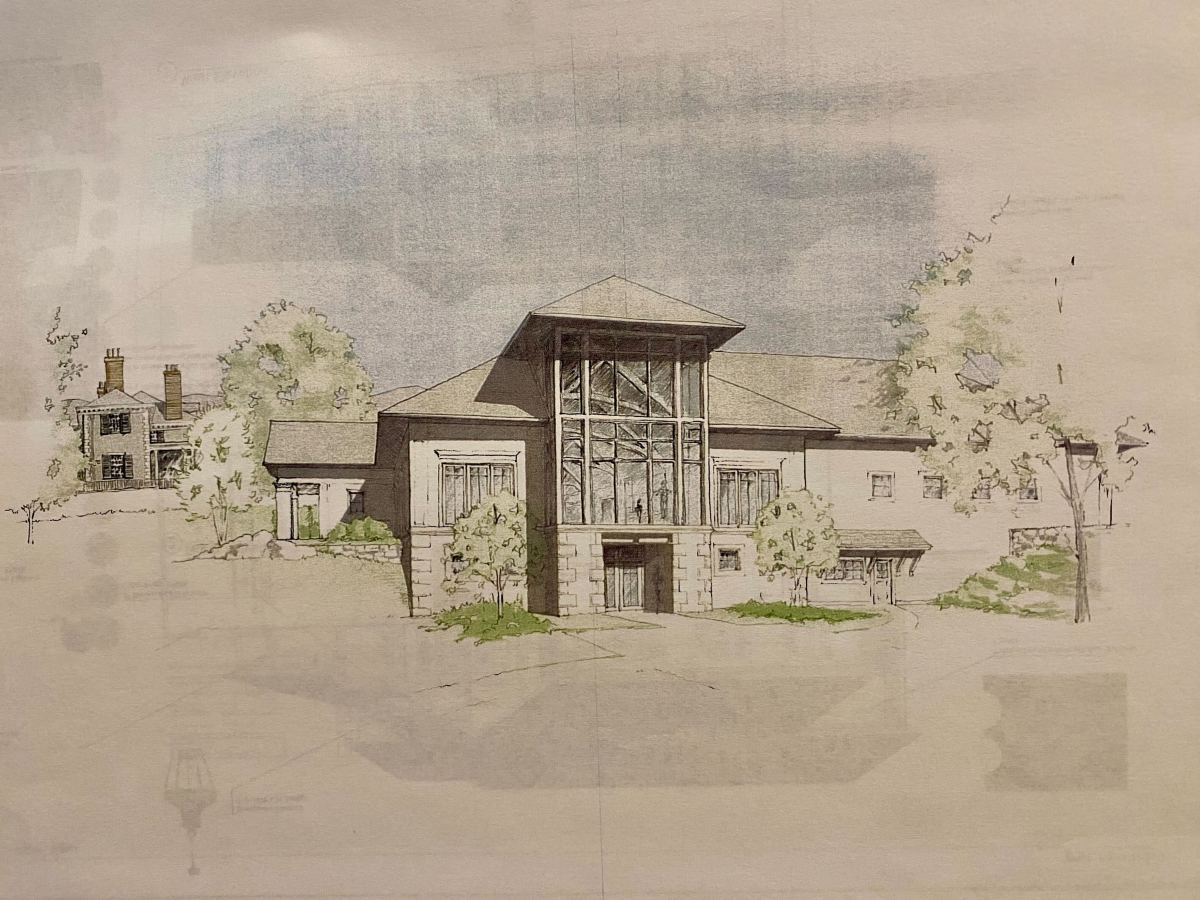 A detailed architectural drawing of a large, two-story building with a prominent glass atrium at the center and surrounded by trees. A smaller house is visible in the background.