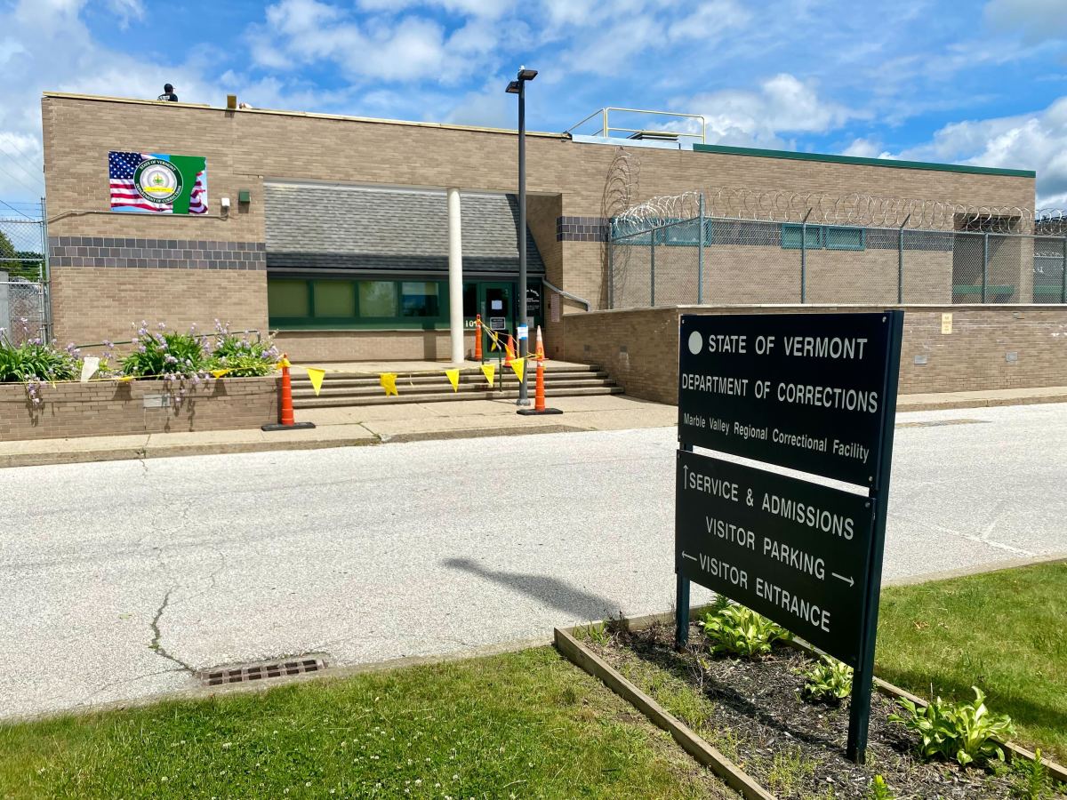 Exterior view of Marble Valley Regional Correctional Facility in Vermont, showing the main entrance with signs indicating admissions, parking, and visitor entrance under a clear sky.