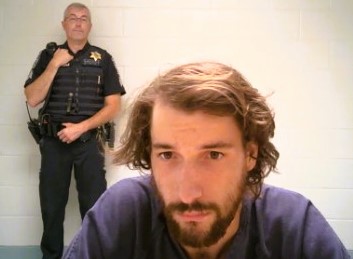A man with a beard is standing in front of a police officer.