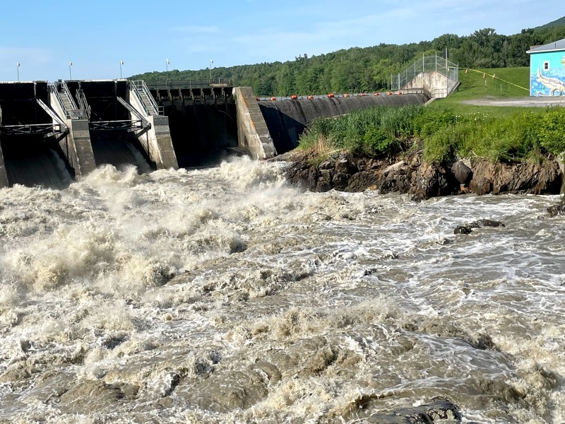 Brown-colored water rushes in front of a dam.