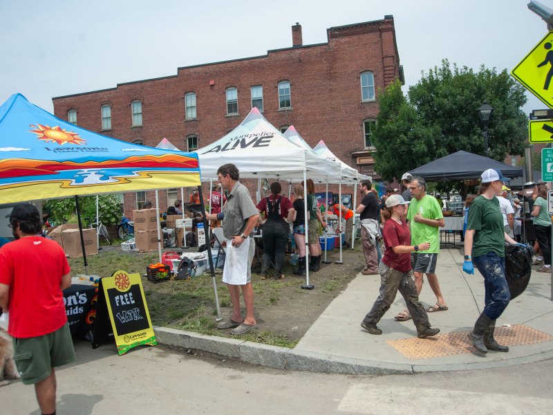 Pop-up tents in front of a brick building as people walk down the sidewalk.