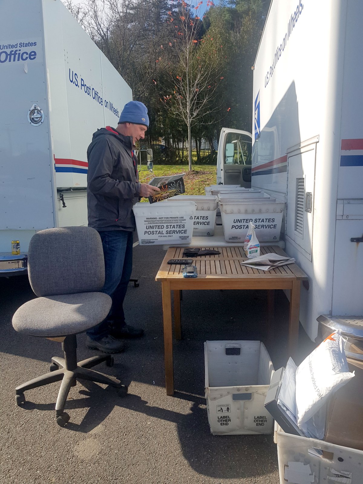A man sorts through mail in front of two mail trucks.