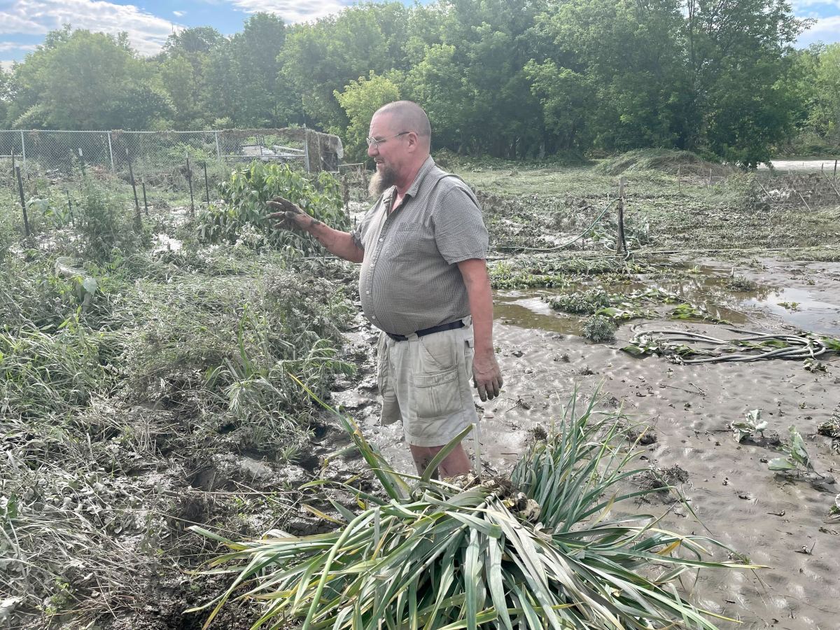 a man standing in a muddy field with plants.