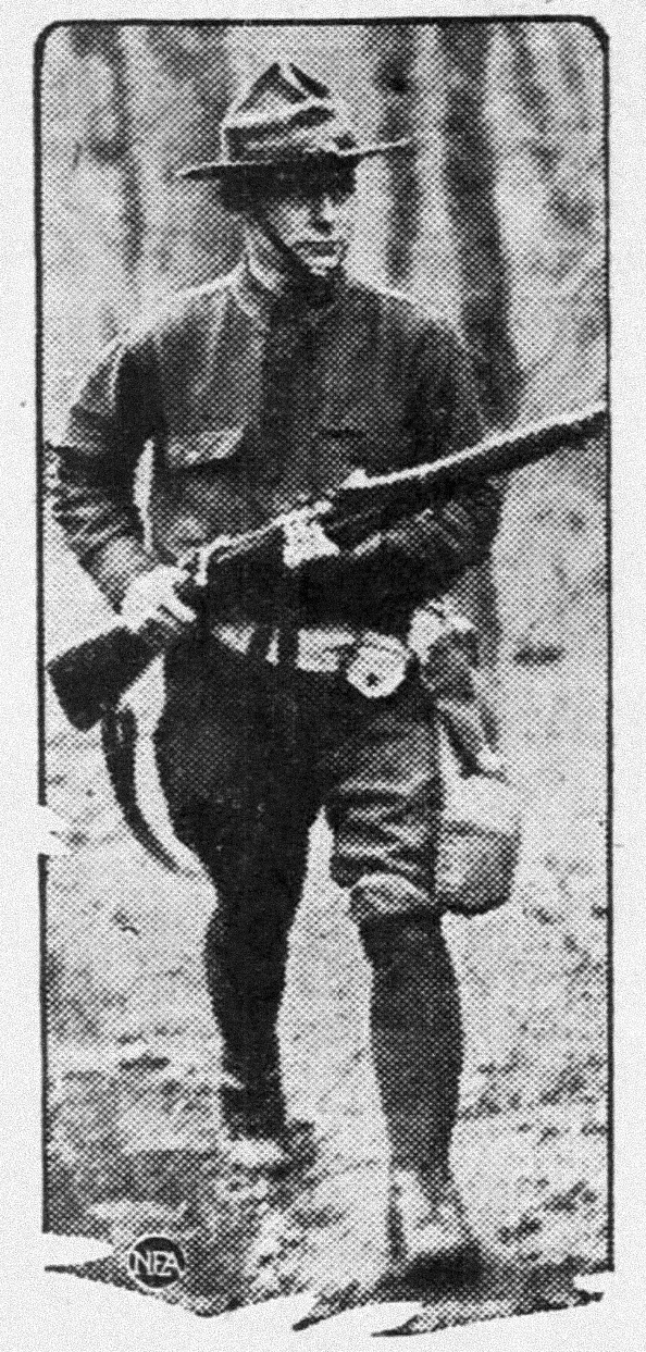 A soldier in historical uniform carrying a rifle and wearing a campaign hat in a wooded area.