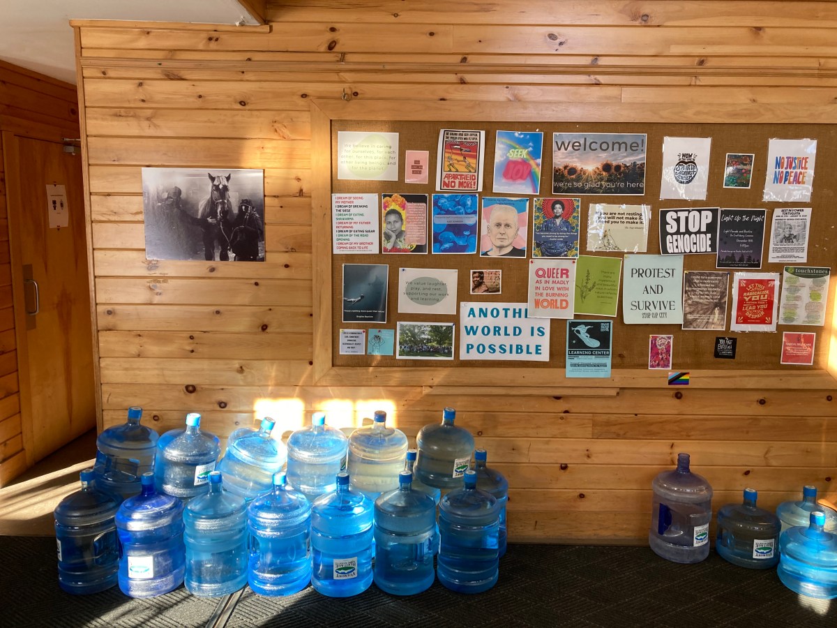 A group of water jugs pushed against a wall under a bulletin board