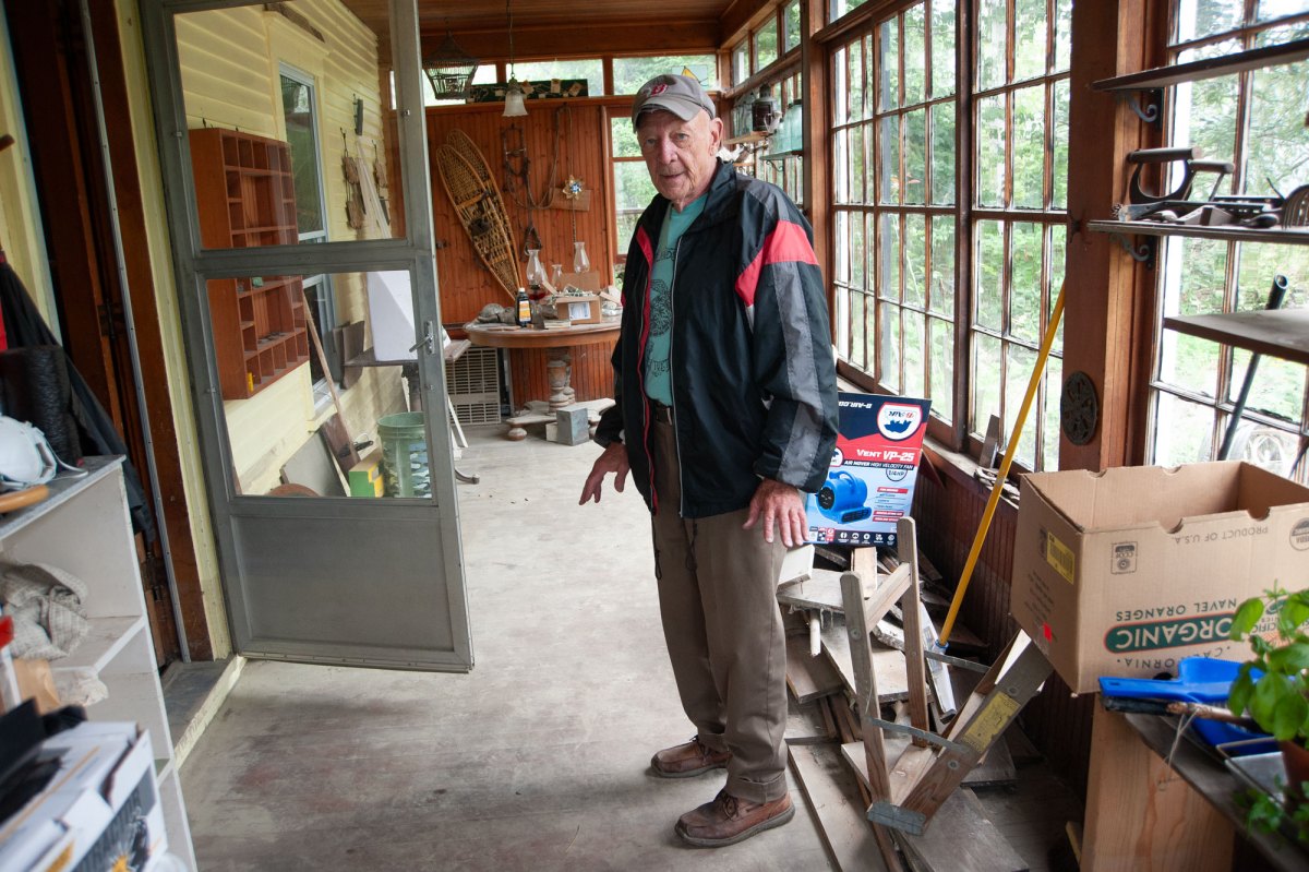 A man in a baseball cap stands on an enclosed porch.